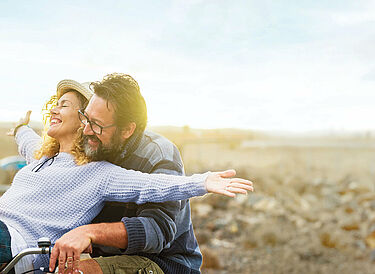 Elderly husband with beard and glasses hugs his smiling wife from behind
